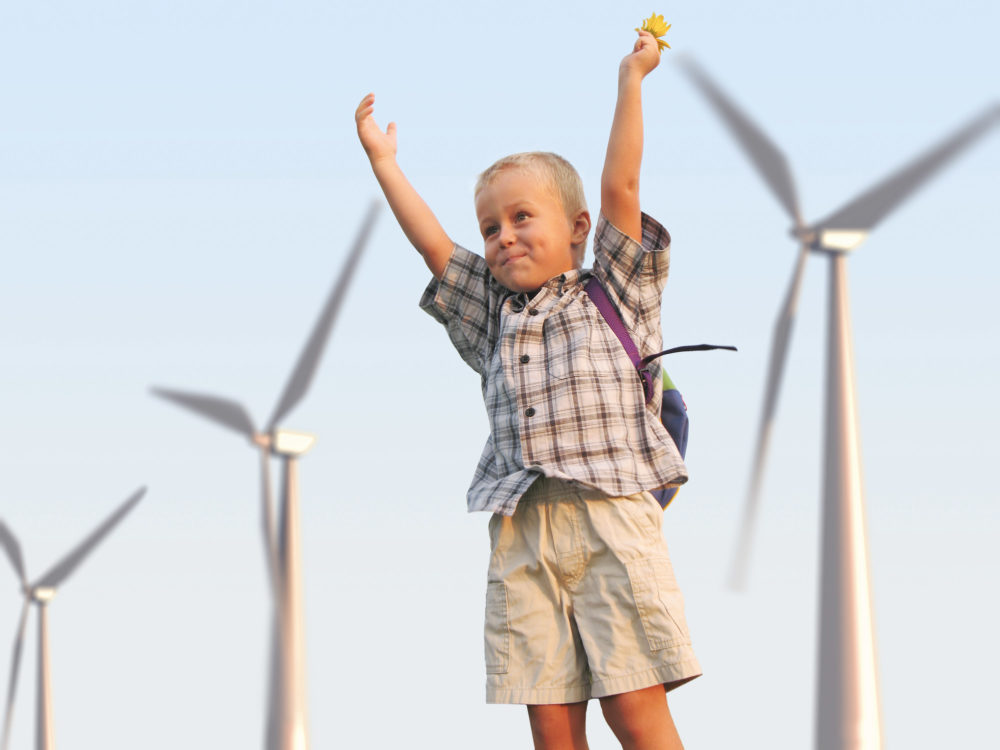 Young boy standing near wind turbine with arms in the air