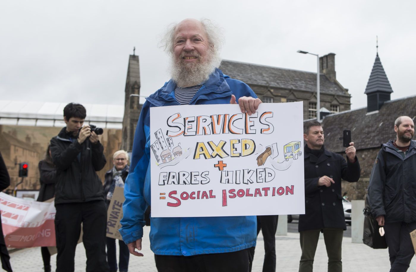 Bus protestor outside Scottish Parliament with "services axed" sign