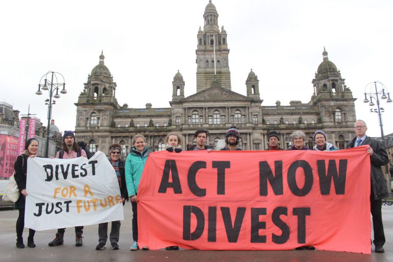 Protestors hold a banner saying 'Act Now Divest' in George Square, Glasgow