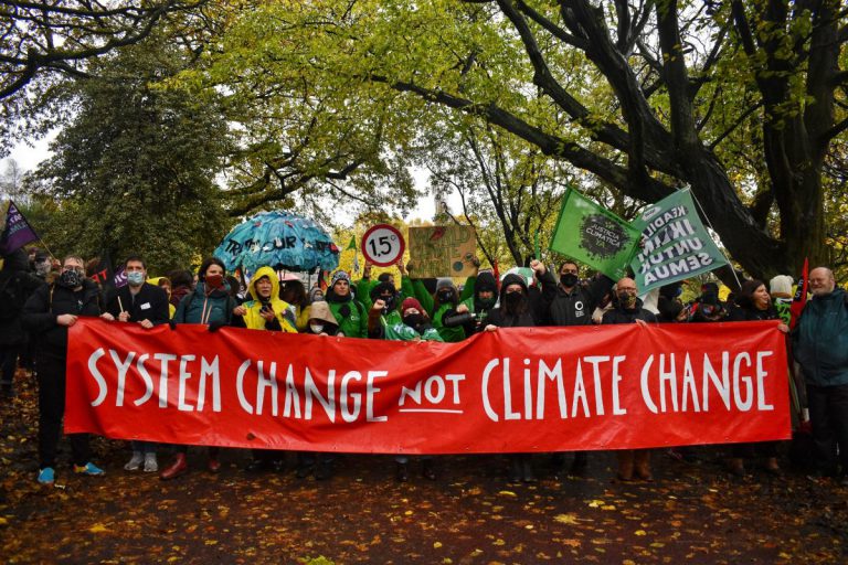 a large group of people holding a red banner with white letters reading system change not climate change