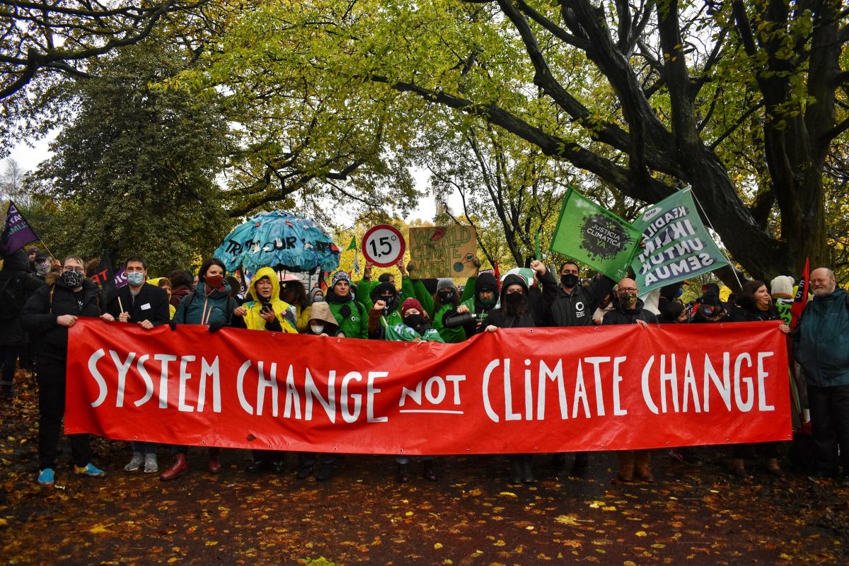 a large group of people holding a red banner with white letters reading system change not climate change