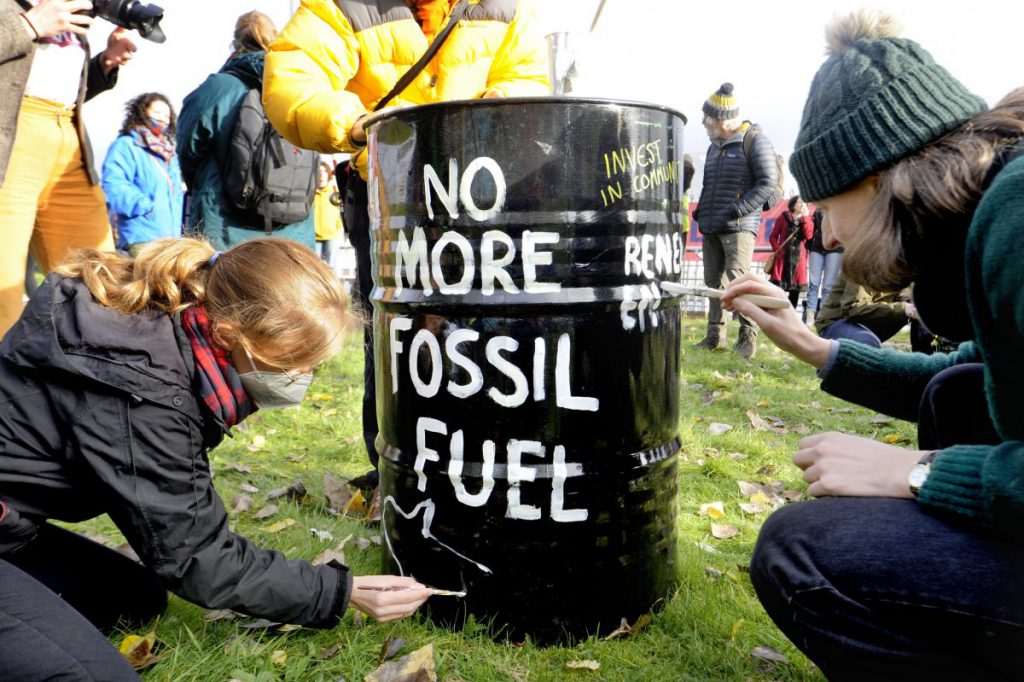 two people painting 'no more fossil fuels' message on an oil drum