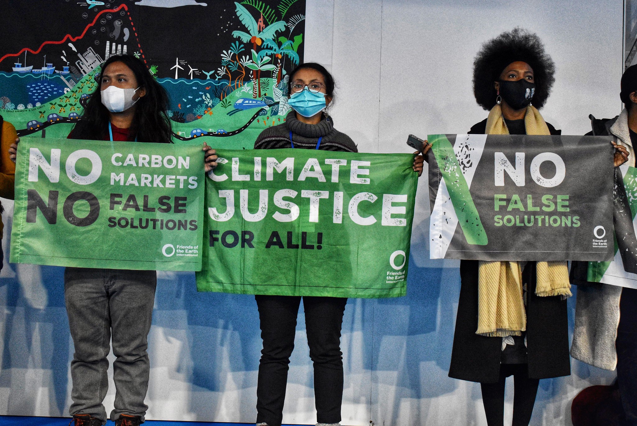 3 people holding signs as part of a 'no carbon markets' protest inside COP26 in Glasgow 2022.