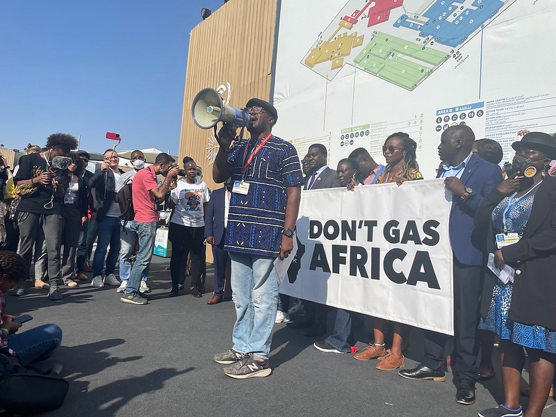 Climate activist with megaphone in front of banner reading "Don't gas Africa"