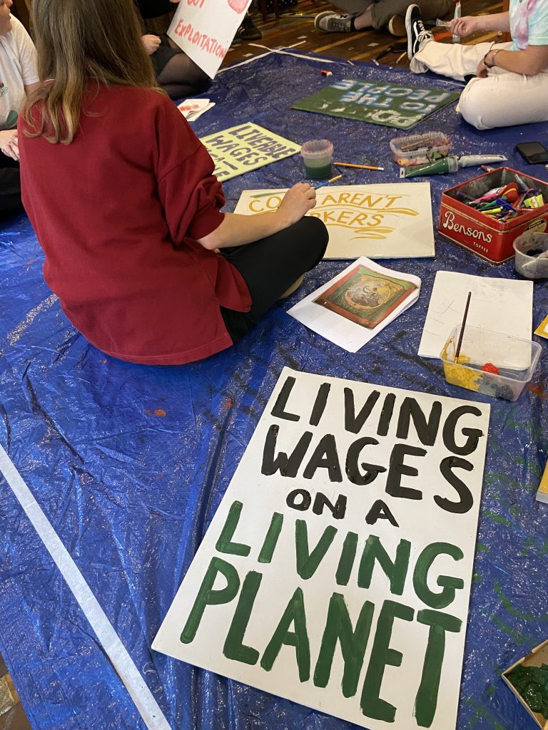 people sitting on the floor painting placards. in the foreground one reads living wages on a living planet.
