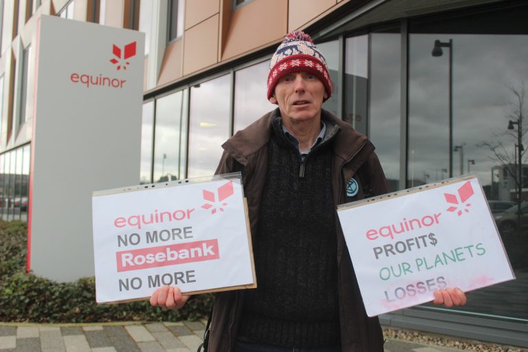 Protesting man outside Equinor offices holding signs saying 'stop rosebank'