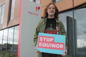 woman holding 'stop equinor' banner outside Equinor offices