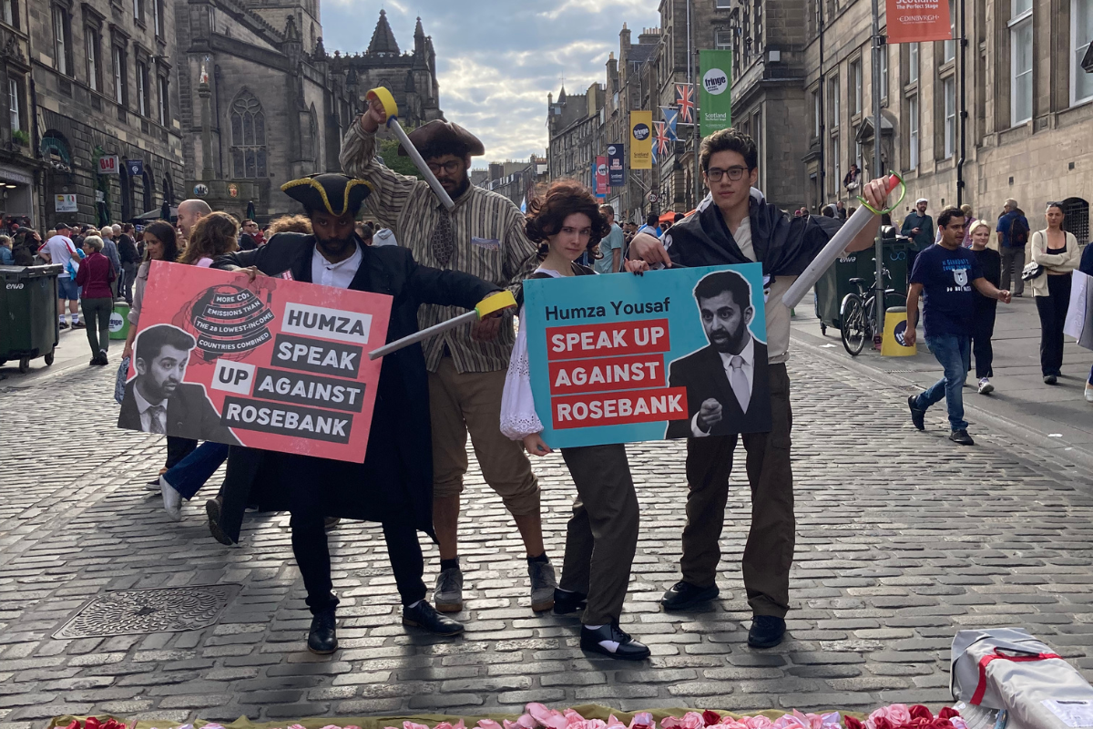 Four fringe performers dressed as pirates with swords hold two placards urging Humza Yousaf to 'Speak out against Rosebank'
