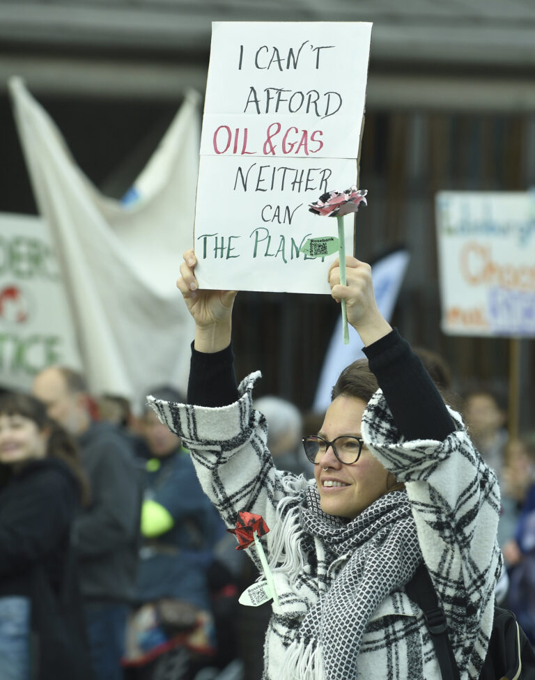 woman holding handwritten sign reading 'i cant afford oil & gas neither can the planet'