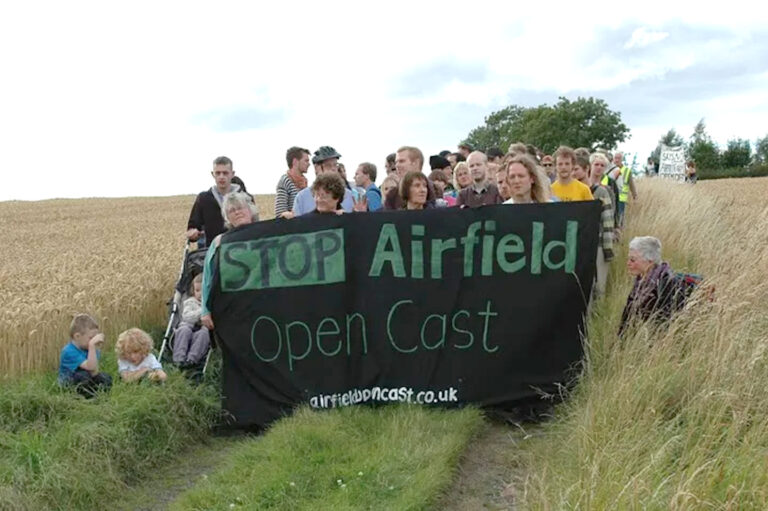 People in a field hold a banner reading 'stop airfield open cast'