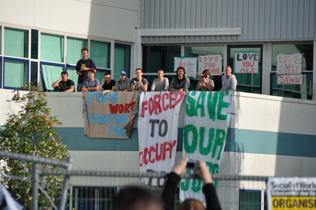 Workers in a factory hold banners reading 'save our jobs'