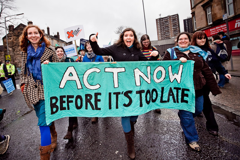 Enthusiastic activists hold a blue banner reading 'act now before it's too late'