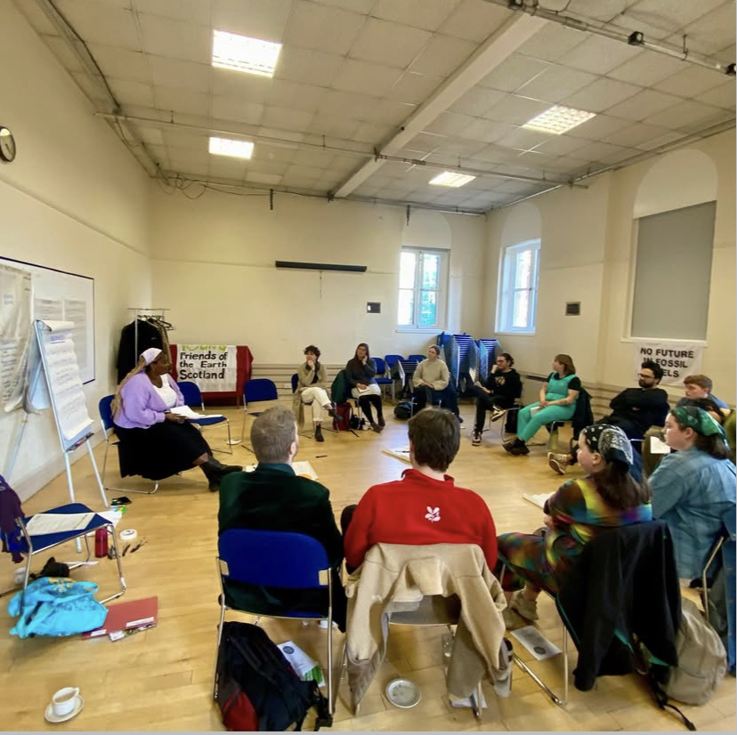 a circle of people around a flip chart with one person presenting