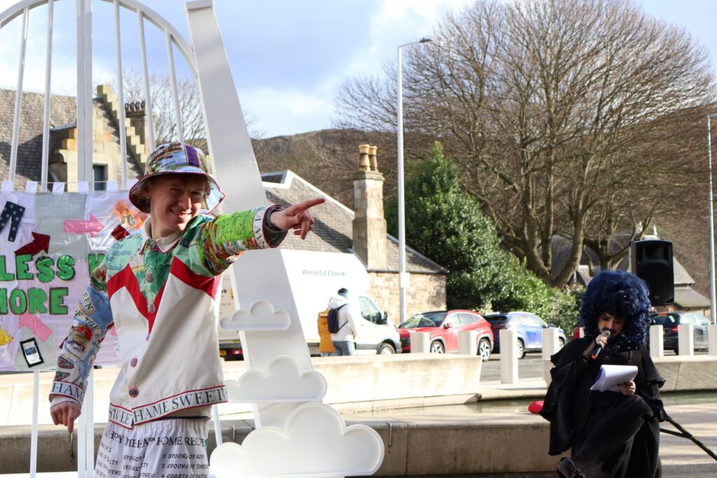 a young man in a funky suit pointing at the camera on a catwalk