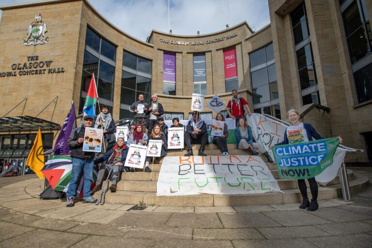 A group of people holding Palestine flags and other signs and placards standing on steps in front of the Royal Concert Hall in Glasgow