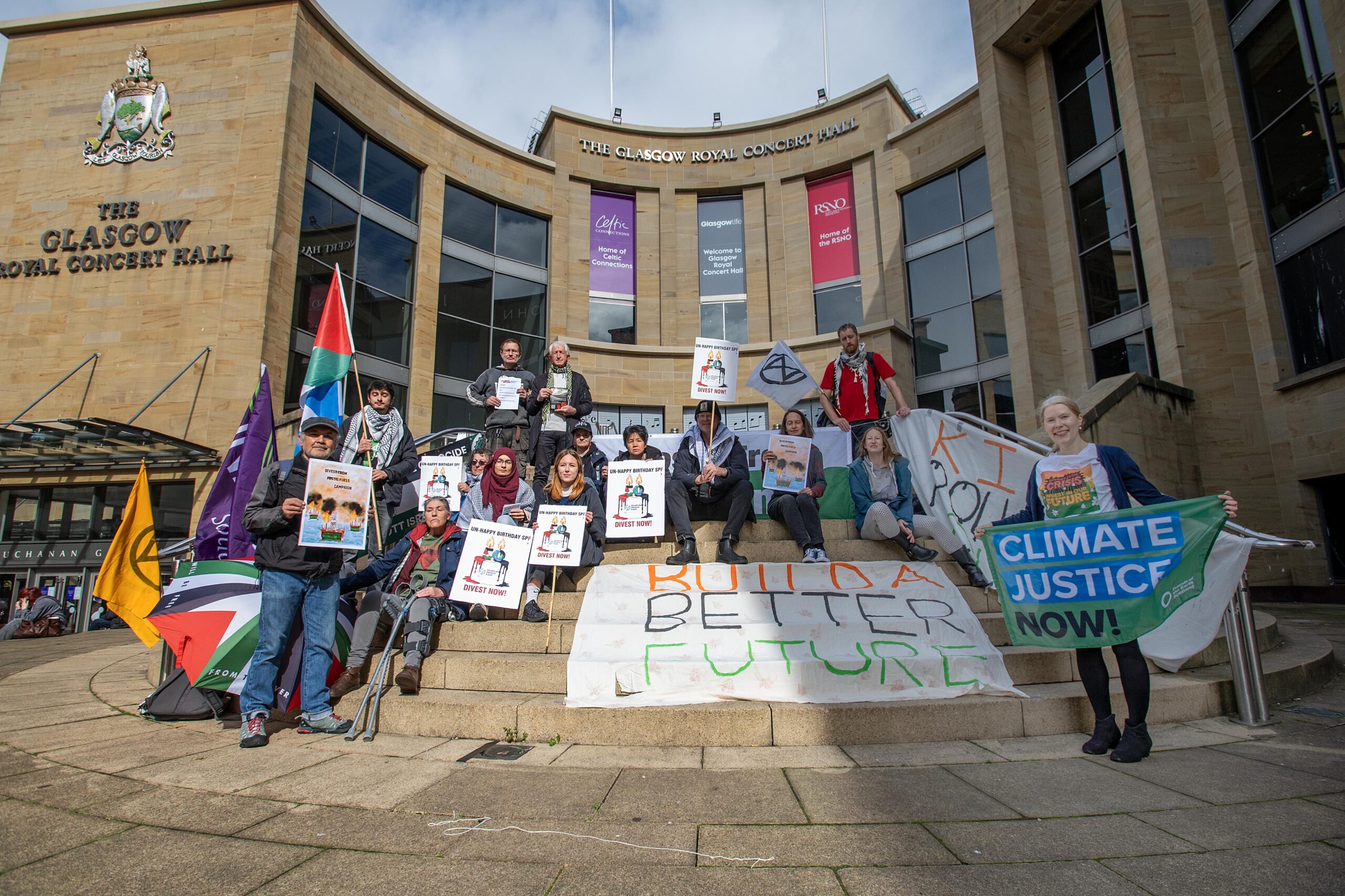 A group of people holding Palestine flags and other signs and placards standing on steps in front of the Royal Concert Hall in Glasgow