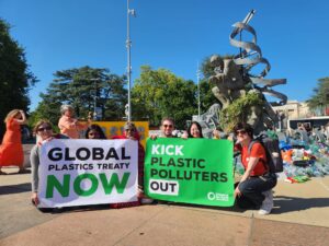 A group of people holding signs that state 'global plastics treaty now' and 'kick plastic polluters out'