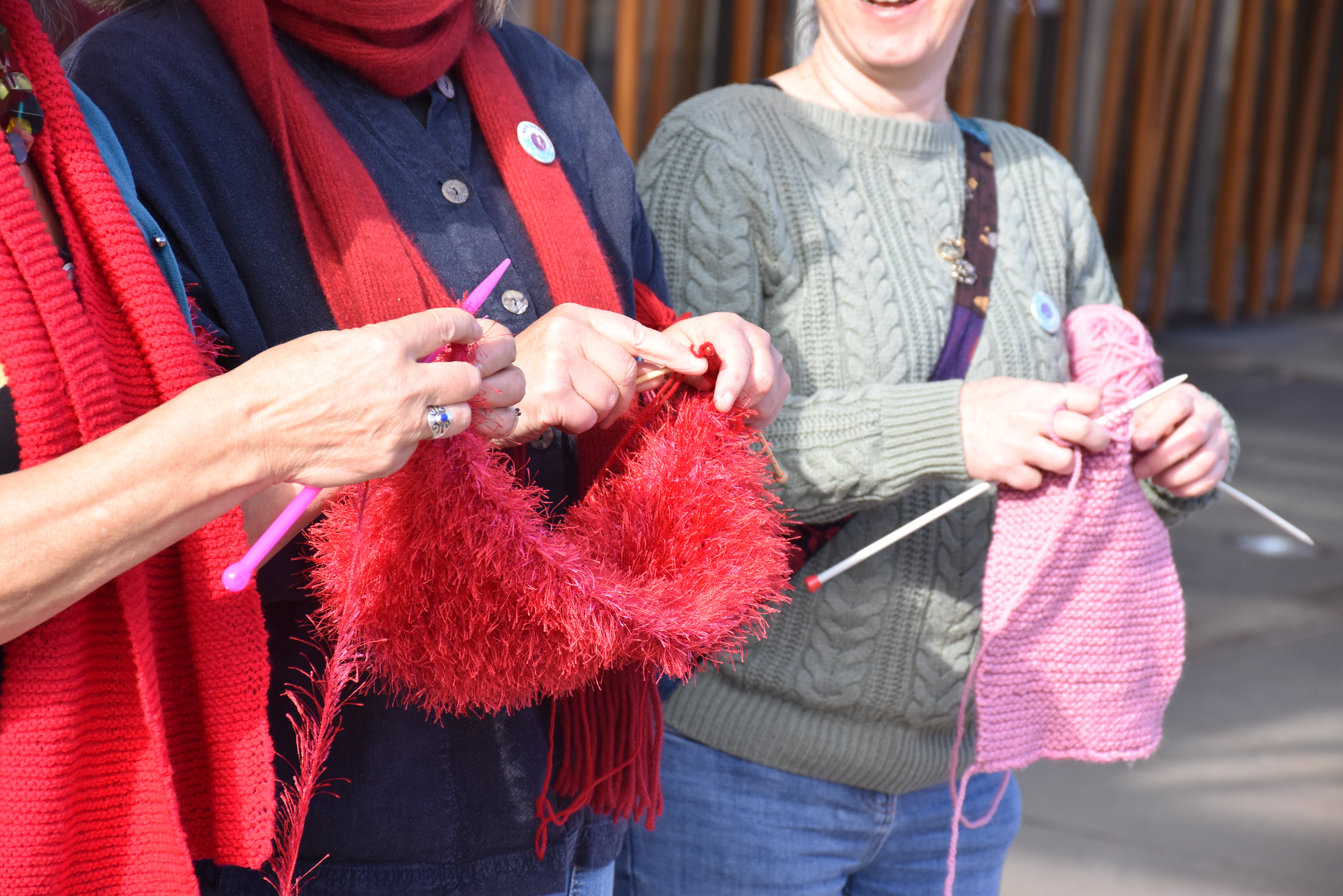 two sets of hands knitting with red wool