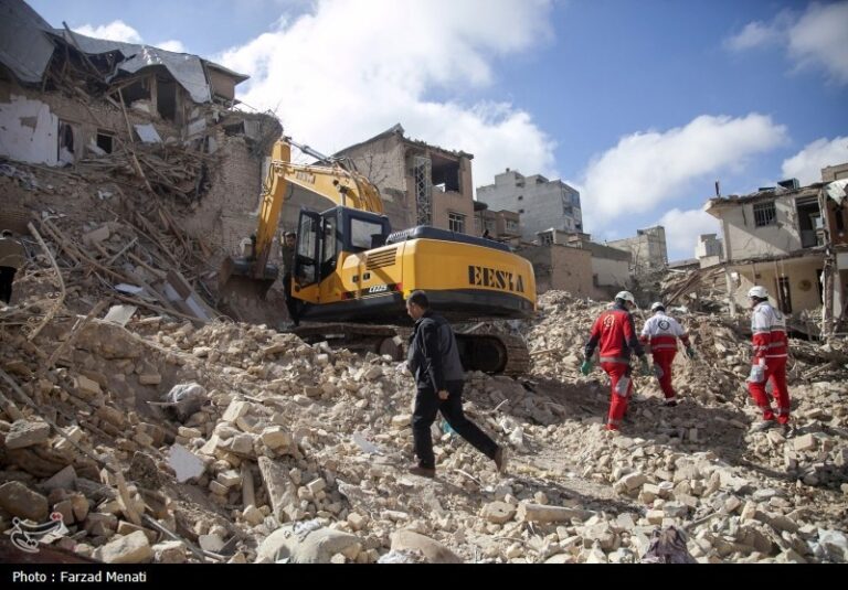 aftermath of missile attack in Iranian neighbourhood. Digger moving rubble with rescuers in foreground