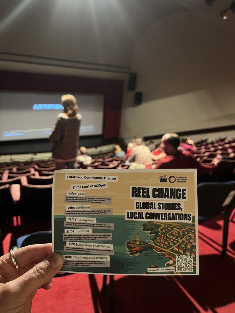 a hand holding up a flyer for peterhead film club in a cinema screem